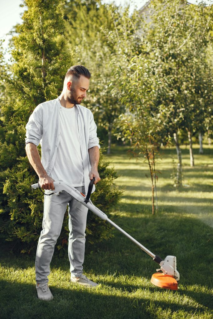 Man using a grass cutter to trim the lawn in a sunny garden. Outdoor gardening activity.